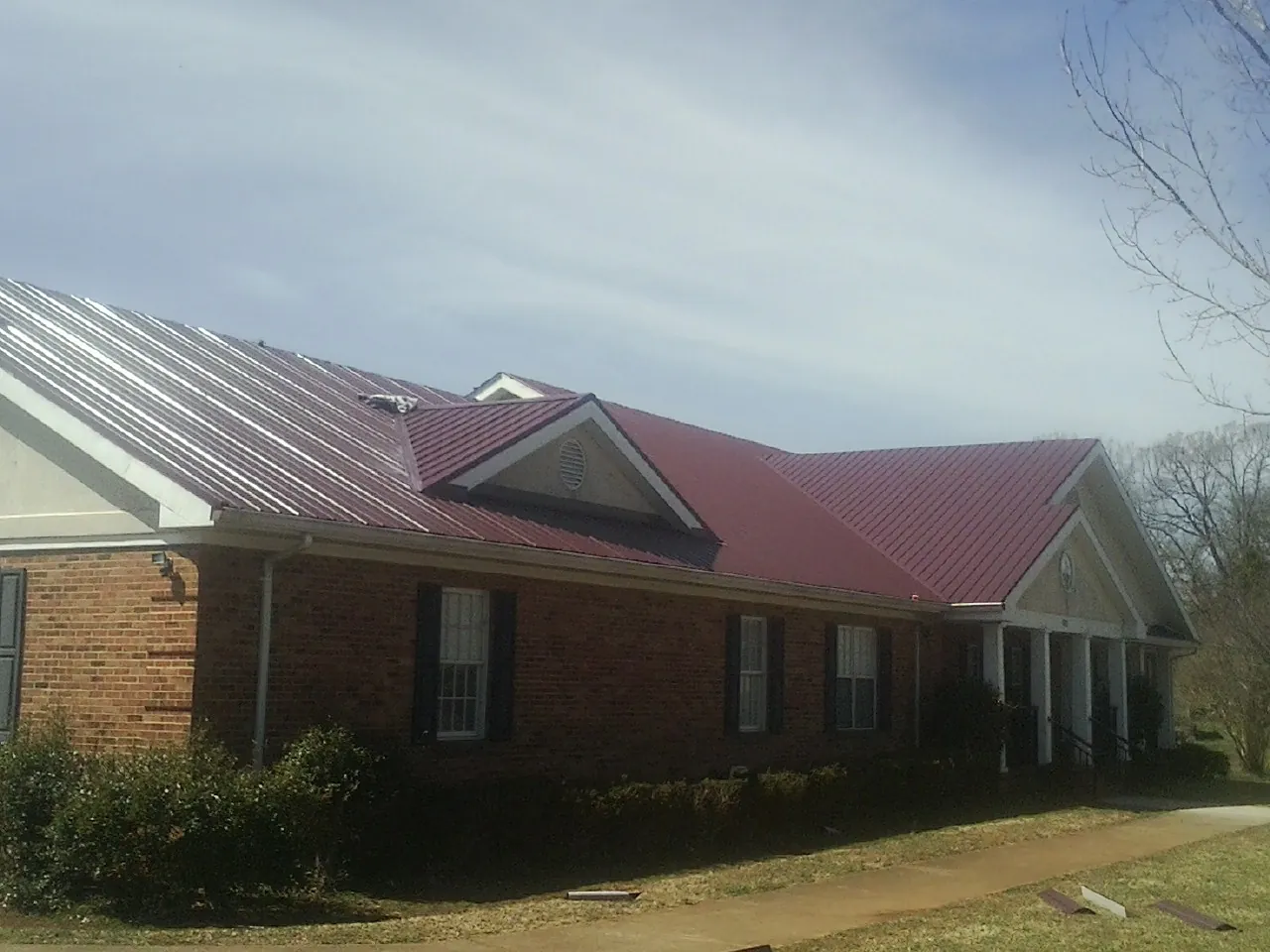 Red metal roof with gabled entries on a long brick building, from a Hail Damage Roof Repair job in Bessemer