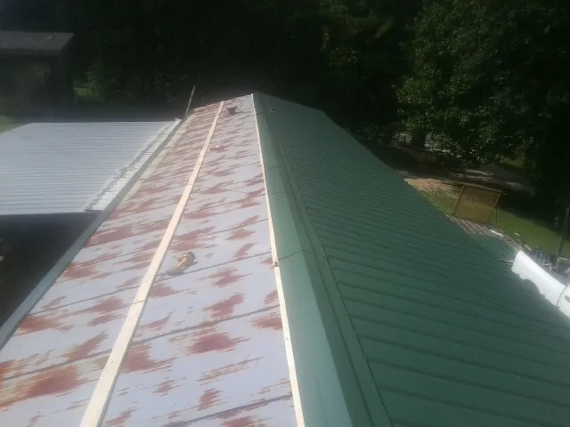 Old rusted panels beside newly installed green metal roofing — Wind Damage Roof Repair by Roofing Brothers in Bessemer