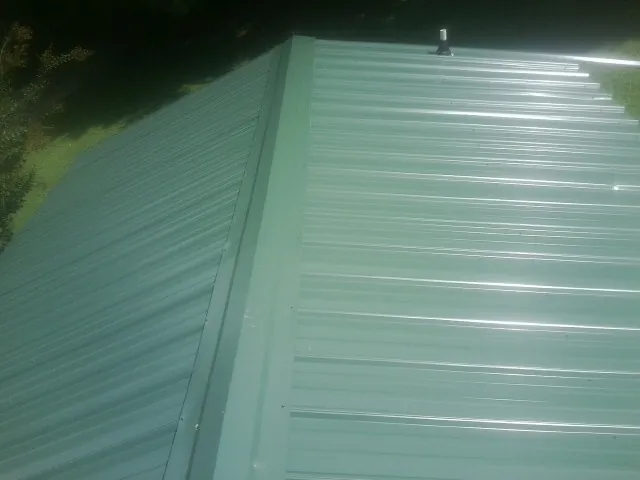 New green metal panels meeting at the ridge of a roof — Flat Roof Repair work by our crew in Bessemer